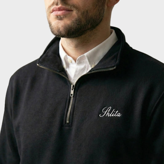 Man wearing a black quarter-zip sweatshirt with 'Shlita' logo on a plain background
